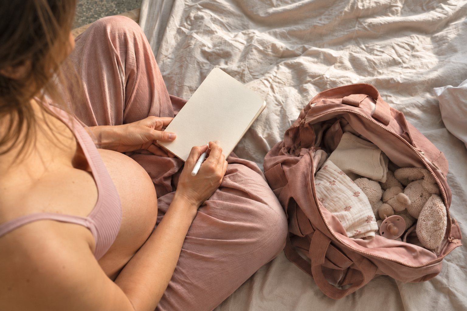 Gravid kvinna som skriver födelseönskningar bredvid packad BB-väska